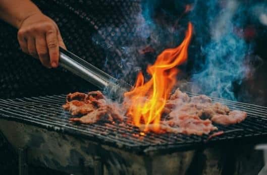 A person holding a metal rod over food on a grill Description automatically generated