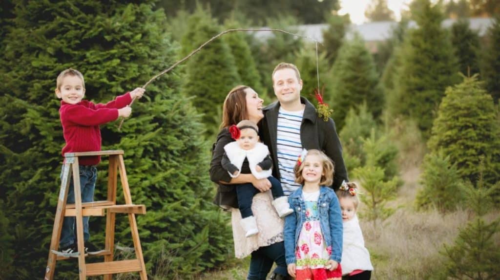 A family smiles for a Christmas photo at a tree farm,