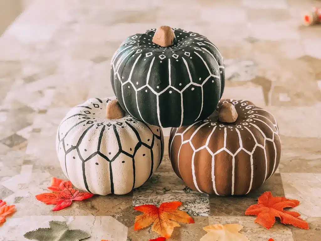 Three knitted or decorated pumpkins sitting on a table with leaves