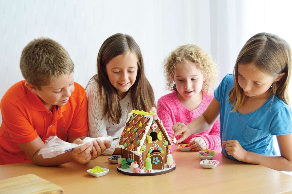 Children happily playing with a gingerbread house